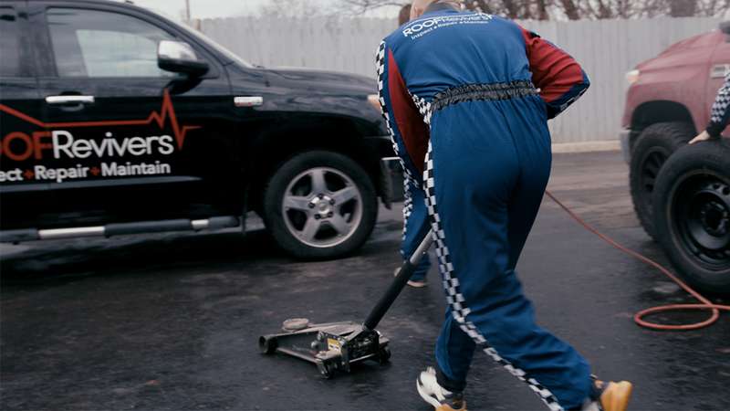 Depicts roofers in racing gear working on a roofing repair truck. 